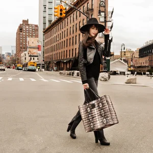 A person crossing the street holding their hat and a hand bag